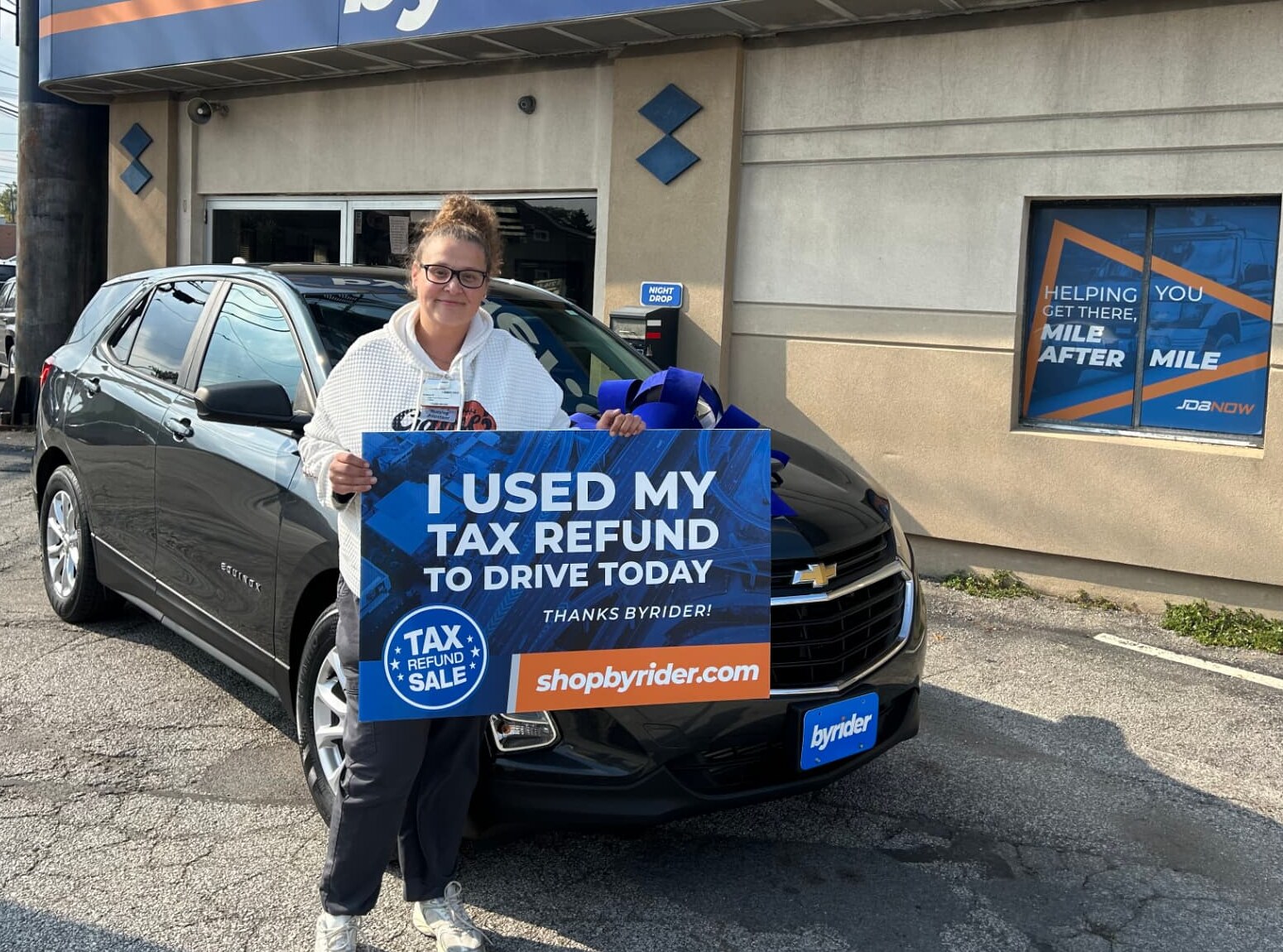 Byrider customer holding an I Used My Tax Refund to Drive Today sign next to her Chevrolet Equinox at a Byrider store in Ohio