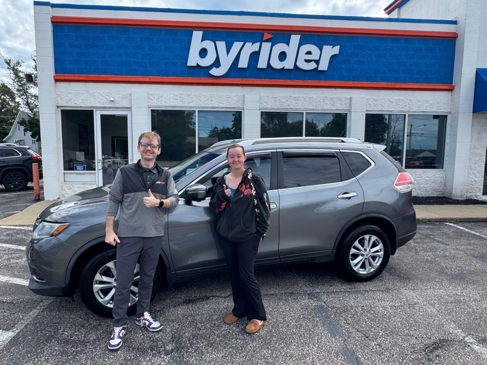 Byrider Ashtabula customer and salesperson beside their used Nissan Rogue at the Ashtabula, Ohio dealership