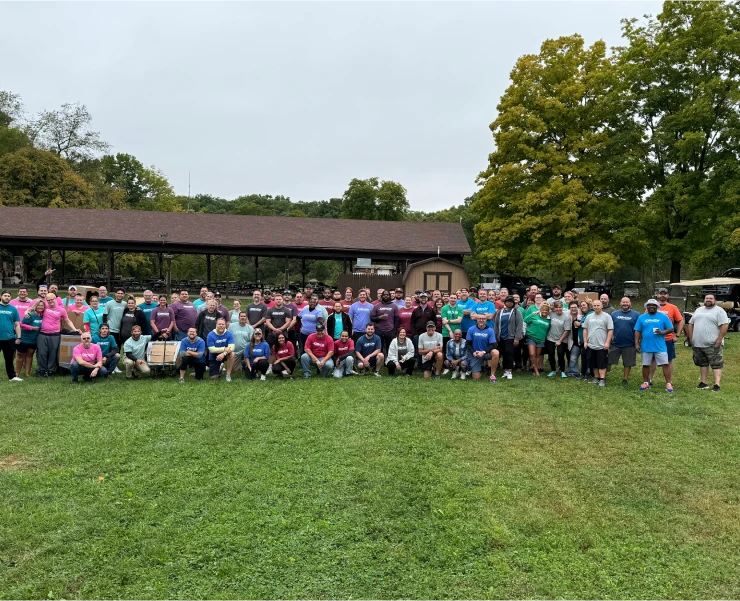The full JDB NOW team gathered for a group photo on a park lawn beside a pavilion